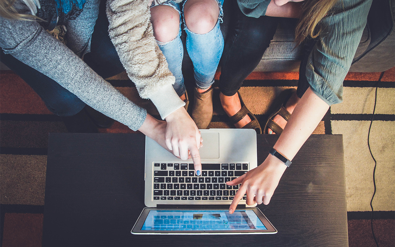 Three sets of arms and hands point to an image on a laptop computer, collaborating.