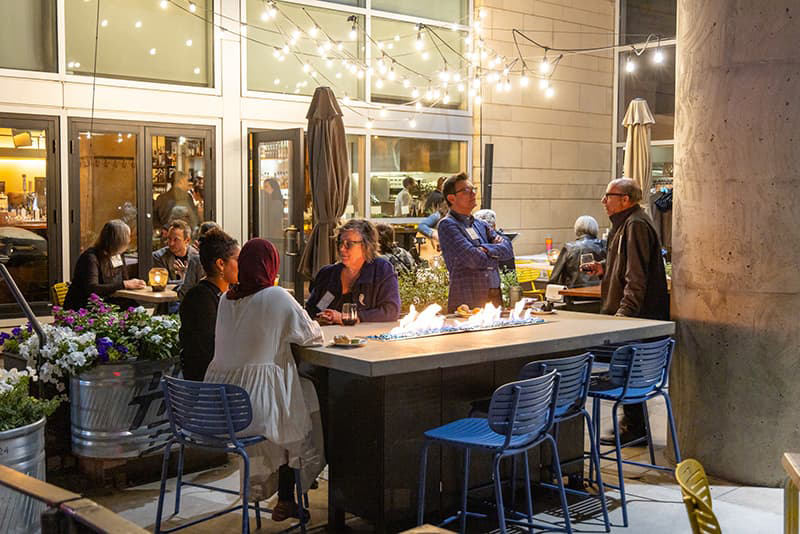 Group of people sit on the Coohills' outdoor patio at night with bistro lighting and a student playing guitar and singing.