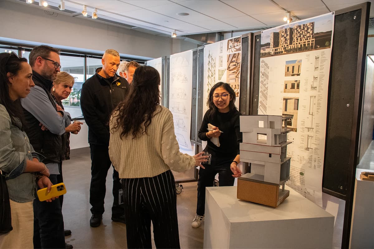 Student stands by a rendering and design posters presenting to a group of people.
