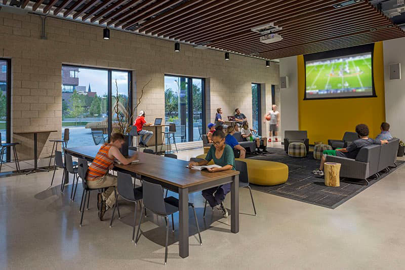 Students throughout the Posner Family Kitchen doing various activities including studying and watching a football game. 