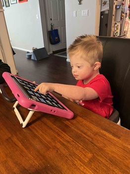 a child sitting at a table and tapping on an aac device