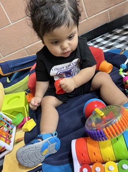 a child sitting on a leckey play pak gazing down at a toy