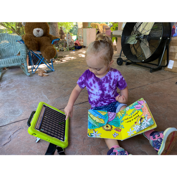 a child reaching for an aac device while holding an open book in her lap